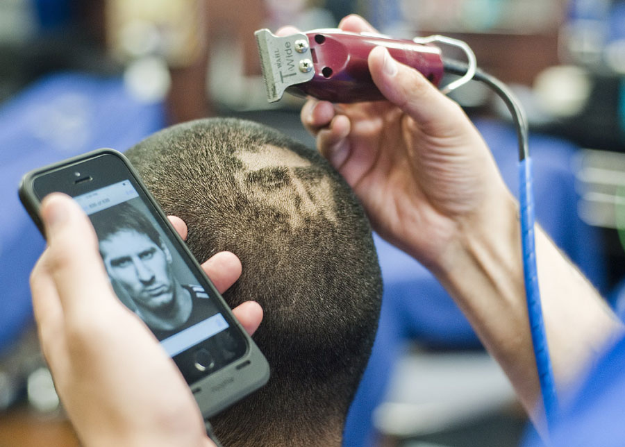 A partir d'une photo affichée sur son mobile, le coiffeur a commencé à ? dessiner ? l'image de Messi sur la tête de son client, lundi 30 juin 2014.