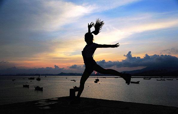 Une touriste saute devant le soleil qui se lève en arrière-plan à Qingdao, dans la Province du Shandong, le 10 ao?t 2015. [Photo / IC]