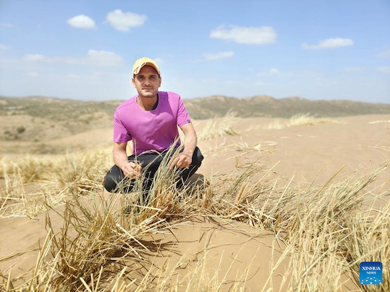 Mohammed Abdulkarem from Yemen poses for a photo with a grass grid he made in northwest China's Ningxia Hui Autonomous Region, June 16, 2023. (Xinhua/Xie Jianwen)