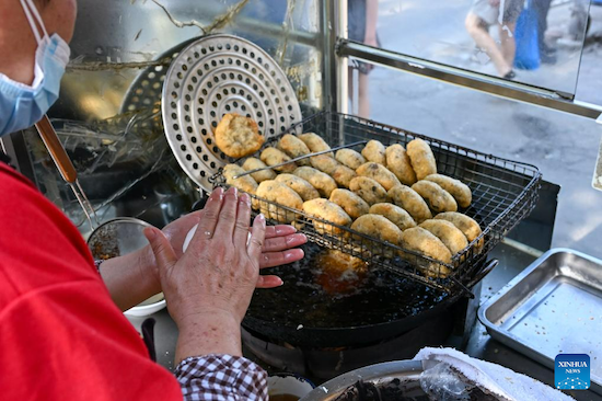 Une dame prépare des zhagao à son stand. Ces beignets de riz glutineux renferment une farce de pate de haricot rouge sucrée. (Xinhua/Sun Fanyue)