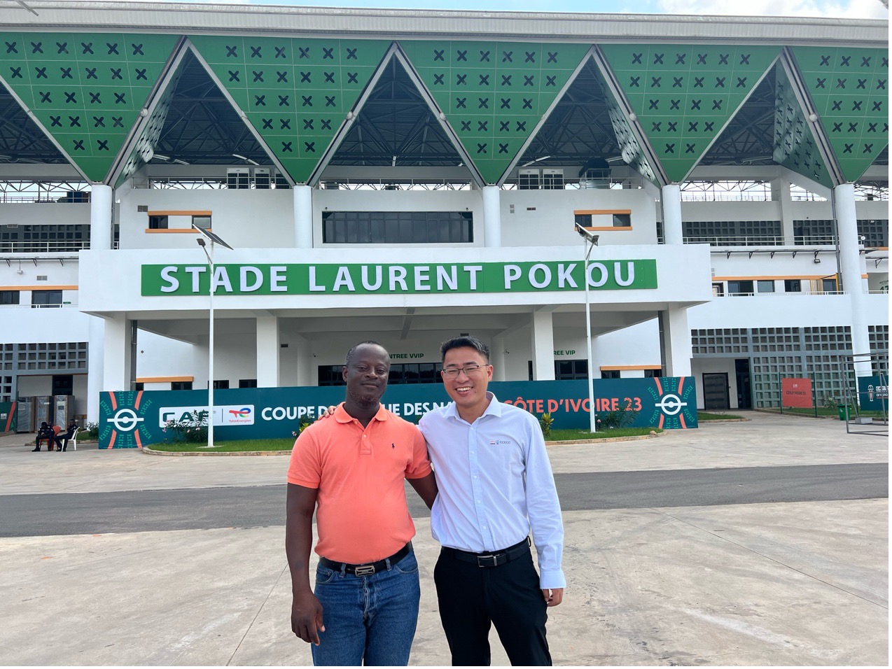 Koffi Lopez, représentant régional de l'Office national des sports à San-Pedro, aux c?tés de son collègue chinois Shi Yongsheng, chef de projet du stade de San Pedro construit par CCECC, devant le stade Laurent Pokou, à San-Pédro, en C?te d'Ivoire. (Photo / le Quotidien du Peuple en ligne)