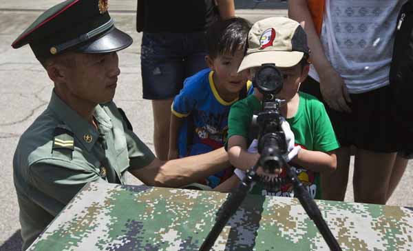 Un jeune gar?on regarde à travers la lunette d'un fusil à c?té d'un soldat de l’Armée de Populaire de Libération (APL) lors d'une journée portes ouvertes à la caserne Shek Kong à Hong Kong le 30 juin 2013. [Photo / agences]