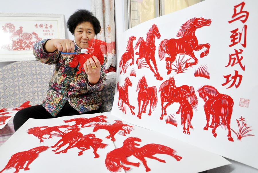 Cai Chun'e agée de 68 ans, une artiste dans l'art du papier découpé à Handan, la province de Hebei, montre son travail sur le thème du cheval, le 23 décembre 2013. Cai a récemment créé plus de 40 oeuvres dans différentes formes pour mettre en avant tout le charme de ce patrimoine culturel immatériel et souhaiter ses bons voeux pour l'Année du Cheval. [Photo : Hao Qunying/Asianewsphoto]