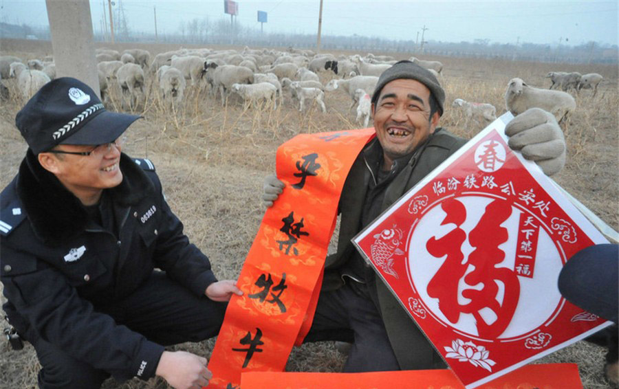 Un policier du bureau de la sécurité publique des chemins de fer du village de Zhangcun, dans la municipalité de Linfen, dans la Province du Shanxi, offre des sentences parallèles de la Fête du Printemps à un villageois, le 16 janvier 2014. [photo / icpress.cn]