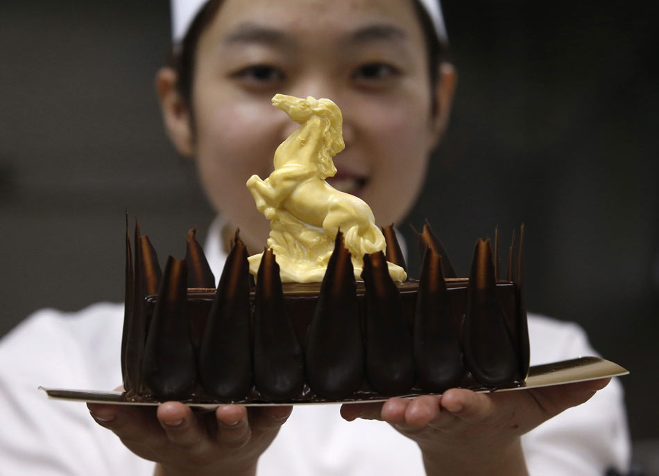 Des chevaux en chocolat blanc à proximité d'un chef en train de faire un gateau au chocolat, lors d'une séance de photos dans une cuisine de Kerry's Pantry à quelques jours du Nouvel An chinois lunaire à Beijing 16 Janvier 2014. [Photo / agences]